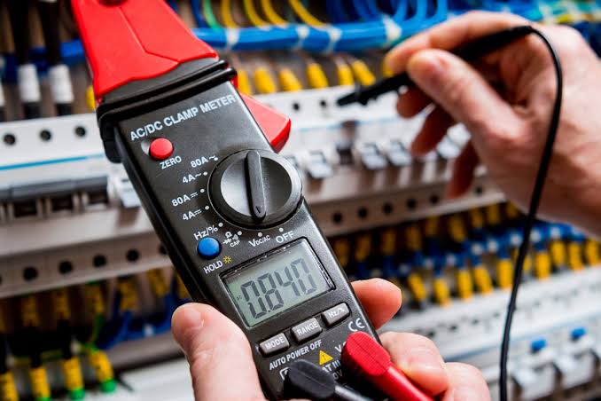 Electrician using an AC/DC clamp meter to test circuits at a consumer unit while fault finding in Fleet, Hampshire